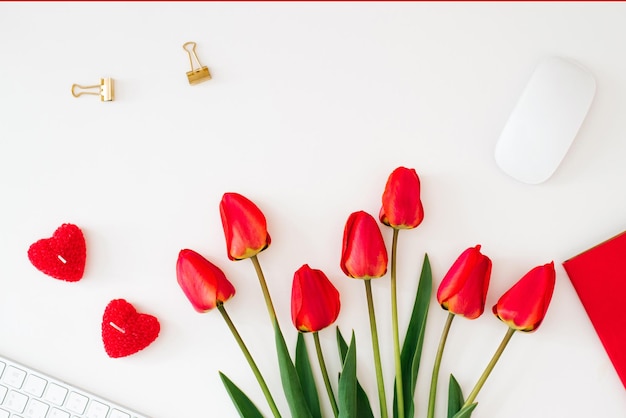 Boeket rode tulpen op het bureaublad met toetsenbord Kladblok en hartjes voor Valentijnsdag