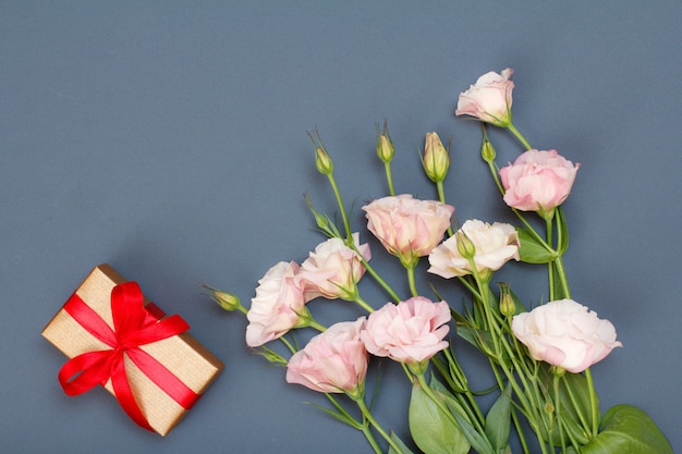 Boeket roze bloemen met bladeren en geschenkdoos gebonden met rood lint op grijze achtergrond. Bovenaanzicht. Viering dag concept.