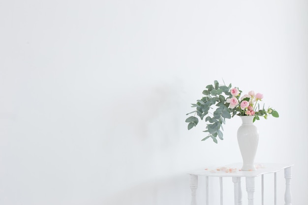 Boeket roze rozen in keramische witte vaas op witte vintage houten plank