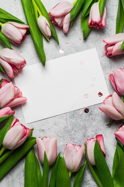 Boeket roze tulpen met wenskaart mock up op grijze steen backround. plat lag met copyspace. wenskaart concept.