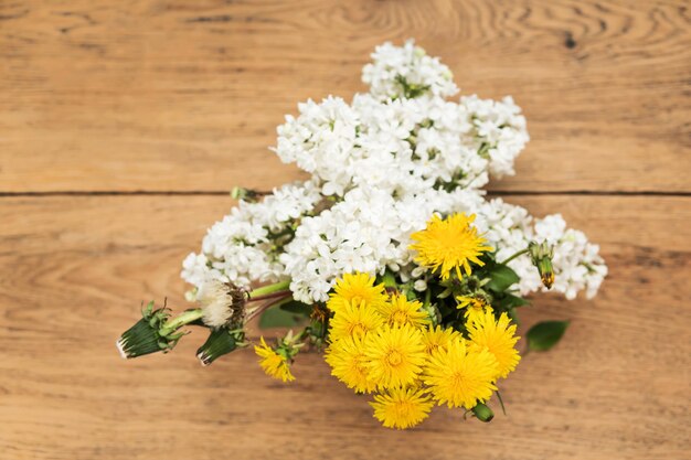 Boeket van bloeiende witte lila en gele paardebloemen met gebladerte op een oude houten tafel, bovenaanzicht