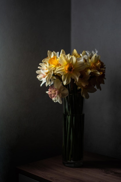 Foto boeket van gele en witte narcissen in een transparante vaas tegen een donkere achtergrond