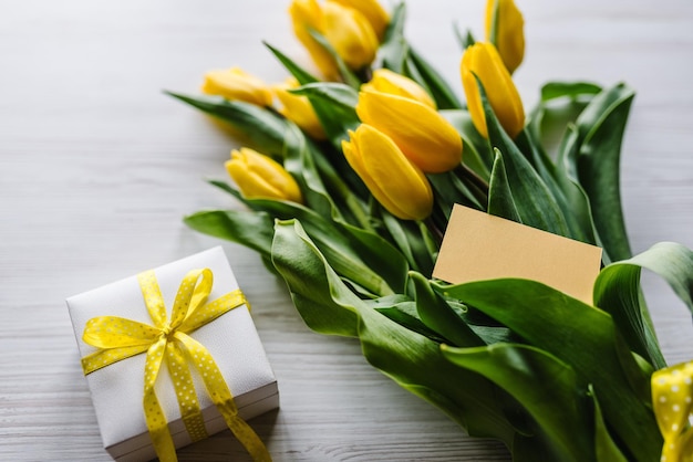 Boeket van gele tulpen met geschenkdoos op houten achtergrond Craft ansichtkaart met ruimte voor bericht bloemen concept wenskaart voor Valentijnsdag Women's Mother's Day Pasen verjaardag
