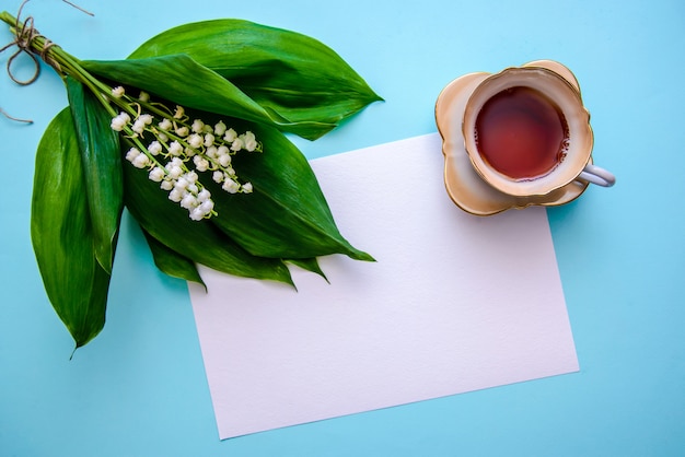 Boeket van lelietje-van-dalen, een kopje thee en een vel papier