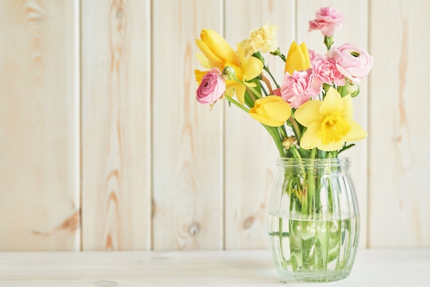 Boeket van lentebloemen: tulpen, anjers, ranunculi en narcissen in vaas op tafel. Moederdag groet