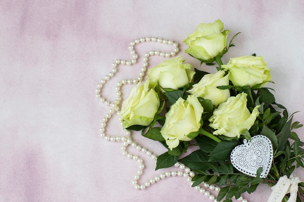 boeket van lichte rozen, witte maaswerk hart en parel kralen op een roze achtergrond