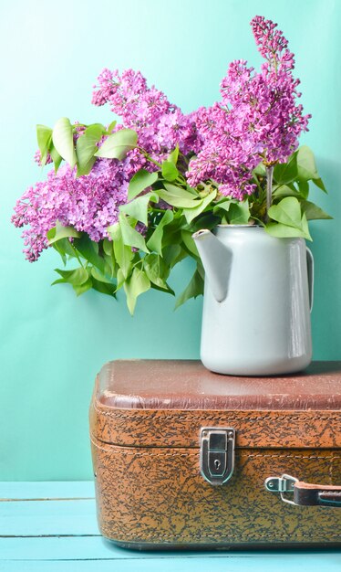 Boeket van lila in een oude geëmailleerde theepot op vintage koffer op blauw.