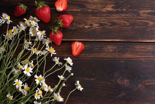 Boeket van madeliefjes met aardbeien op een donkere houten achtergrond, zomer concept, kopieer ruimte, close-up.