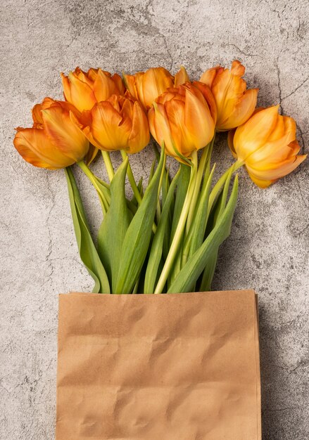 Boeket van oranje tulpen in ambachtelijke verpakking op een betonnen grijze tafel, bovenaanzicht