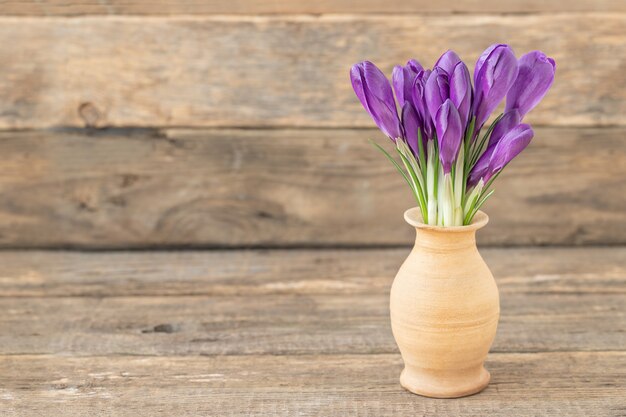 Boeket van paarse krokusbloemen in klei bruine vaas op een houten geweven bruin