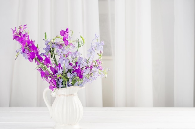 Boeket van paarse lupine bloemen in een jag op witte houten tafel