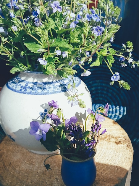 Boeket van paarse veldbloemen in witte porseleinen vaas blauwe ronde rieten plaat houten achtergrond