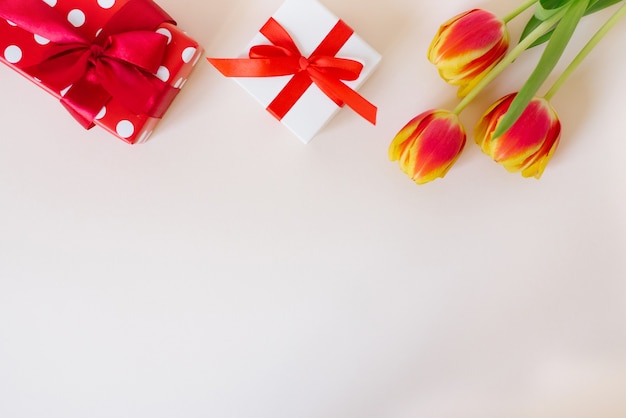 Boeket van prachtige lente tulpen in vaas en geschenkdoos op tafel tegen lichte achtergrond.