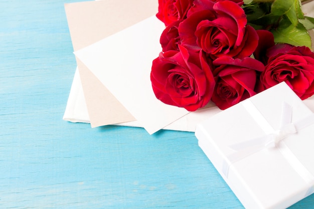 Boeket van rode rozen Witte geschenkdoos schoon blad, blauwe houten achtergrond. Kopieer ruimte. Romantisch cadeau voor Valentijnsdag vakantie
