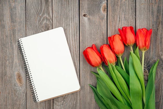 Boeket van rode tulpen en notebook op een houten achtergrond bovenaanzicht