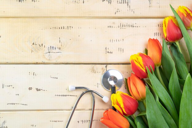 Boeket van rode tulpen op een beige houten ondergrond en een medische stethoscoop, kopieerruimte