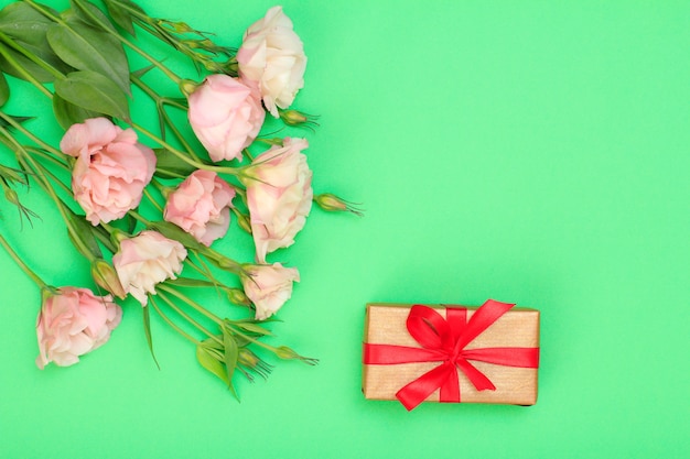 Boeket van roze bloemen met bladeren en geschenkdoos met rode linten op groene achtergrond. Bovenaanzicht. Viering dag concept.