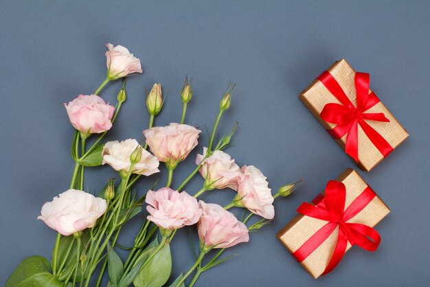 Boeket van roze bloemen met bladeren en geschenkdozen met rode linten op grijze achtergrond. Bovenaanzicht. Viering dag concept.