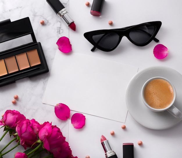 Boeket van roze rozen, kopje koffie, zonnebril, concealer en lippenstift op witte tafel.