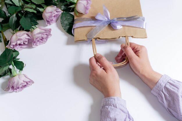 Boeket van violette rozen en vrouwenhanden met boodschappentas op de witte achtergrond, bovenaanzicht.