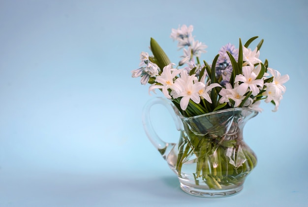 Boeket van witte bloemen in een glazen vaas op een blauwe achtergrond