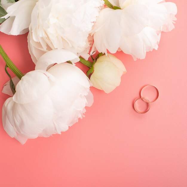 Boeket van witte pioenrozen met trouwringen op een roze achtergrond