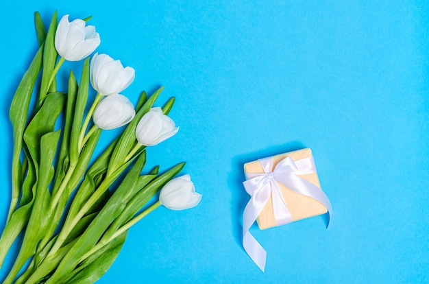 Boeket van witte tulpen met een geschenkdoos op een blauwe tafel. Plat leggen, ruimte, voorjaar concept, plaats voor tekst kopiëren. Uitzicht van boven.