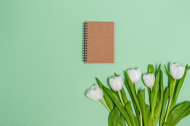 Boeket van witte tulpen met een notitieboekje voor aantekeningen op een groene achtergrond. Lente concept, kopie ruimte, plat leggen, plaats voor tekst. Banner. Uitzicht van boven.