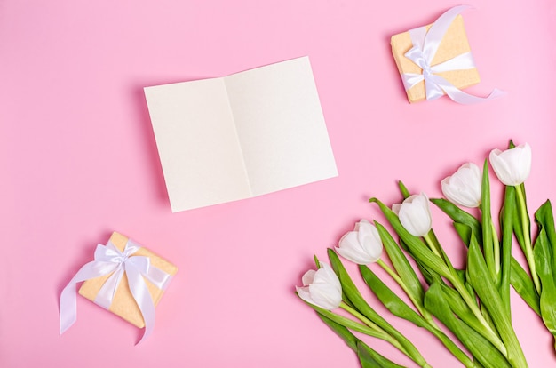 Boeket van witte tulpen met een wenskaart en geschenkdozen op een roze tafel