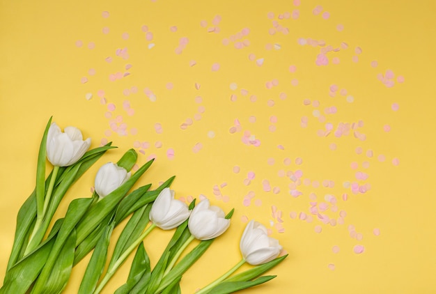 Boeket van witte tulpen met roze confetti op een gele muur