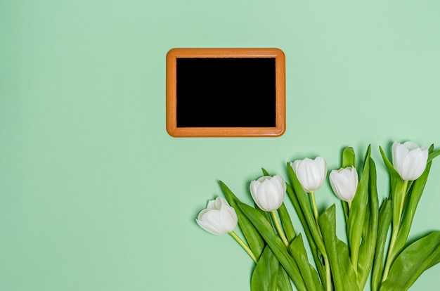 Boeket van witte tulpen op een groene tafel met een tekentafel en plaats voor tekst. Lente concept, kopie ruimte, plat leggen. Uitzicht van boven.