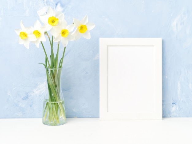 Boeket verse bloemen, wit frame op tafel, tegenover blauw getextureerde betonnen muur.