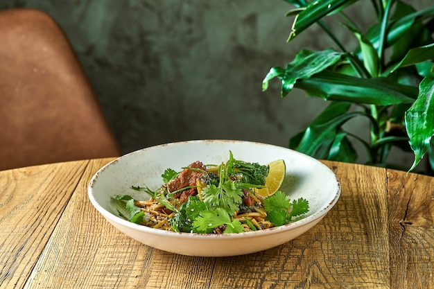 Boekweit udon wok noedels met kalfsvlees, koriandersaus en paksoi in een wit bord. Close-up, selectieve focus