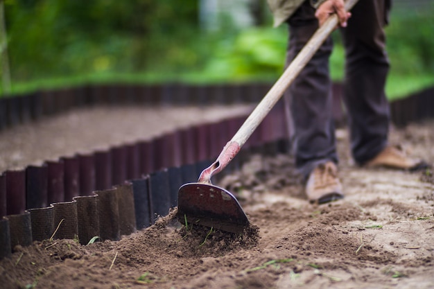 Boer cultiveert land in de tuin met handgereedschap Bodem losmaken Tuinconcept Landbouwwerkzaamheden op de plantage