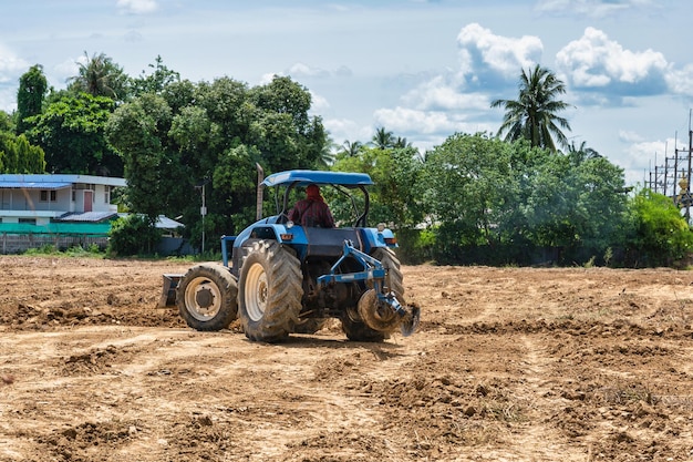 Boer die een blauwe tractor bestuurt om gecultiveerde grond in landbouwgebied te ploegen