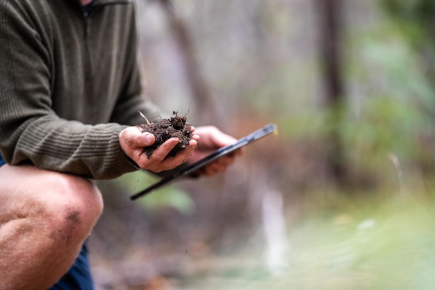 boer met een hoed die zonne-intelligent is met behulp van technologie en een tablet en telefoon in een veld die een bodem- en plantmonster in het veld bestudeert