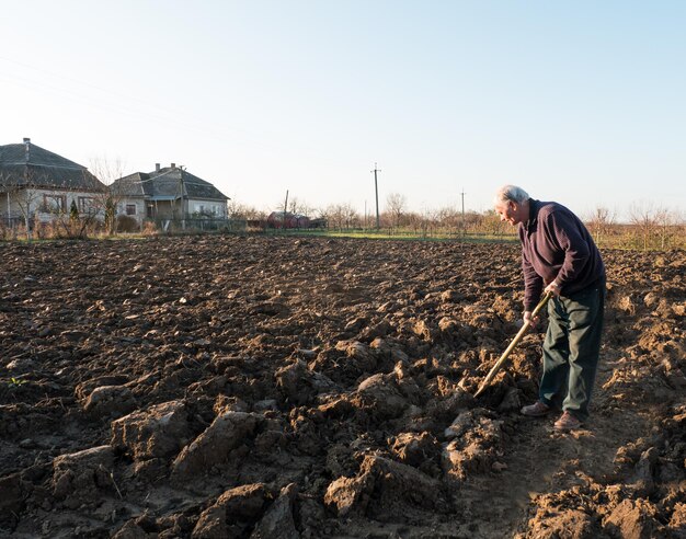 Boer staat met een schop op het veld. Lente tijd. Begin voorjaarswerk op het veld