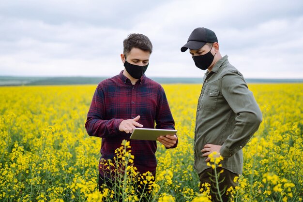 Foto boeren met tablet in het veld boeren met medische maskers bespreken landbouwkwesties op het veld