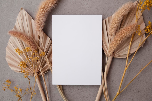 Boheemse blanco uitnodigingskaart omgeven door natuurlijk gedroogd palmblad en grassen bruiloft en feest...