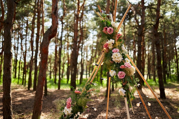 Bohemian tipi arch made of wooden rods decorated with pink roses candles on carpet pampass grass