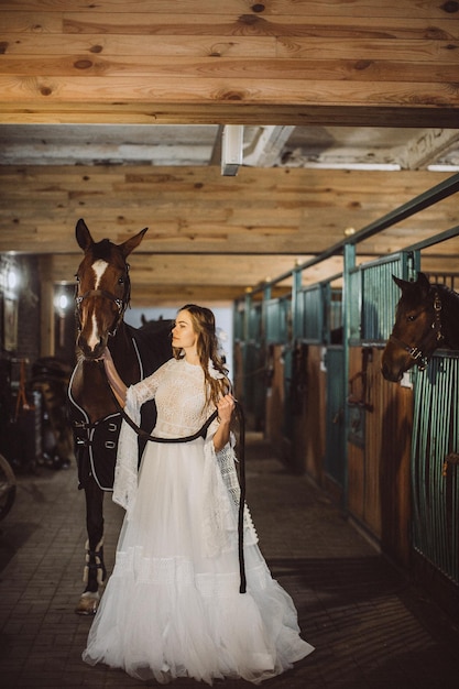 A boho bride poses with a horse in a stable