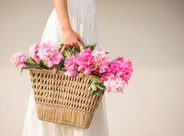 Boho girl holding pink peonies in straw basket.