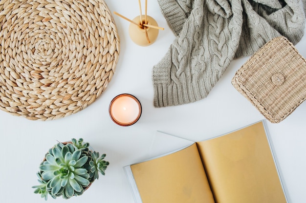 Boho style modern minimal home workspace desk with notebook, succulent, knitted plaid, candle, aroma sticks, straw wicker and napkins on white surface