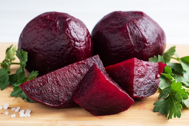 Boiled beets whole and cut on a cutting Board with parsley leaves on a white background