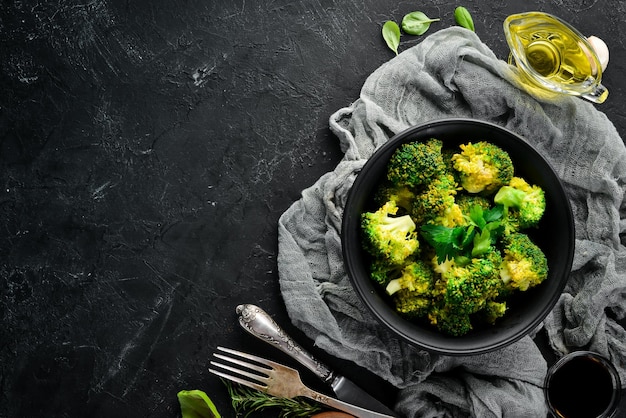 Boiled broccoli in a black plate On a black background Top view Free space for your text