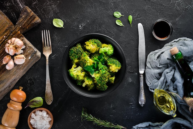 Boiled broccoli in a black plate. On a black background. Top view. Free space for your text.