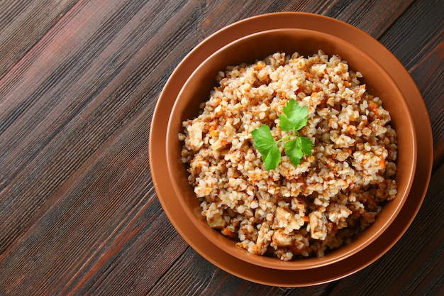 Boiled buckwheat in a bowl with pieces of chicken meat and cilantro on a brown wooden table.