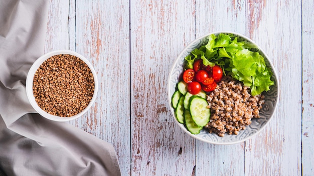 Boiled buckwheat pieces of fresh vegetables and herbs in a bowl on the table top view web banner