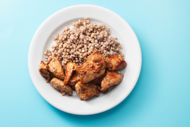 Boiled buckwheat with chicken in sauce on white plate on blue table