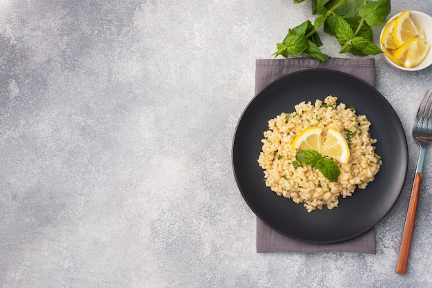 Boiled bulgur with fresh lemon and mint on a plate. A traditional oriental dish called Tabouleh. Gray concrete background top view, copy space